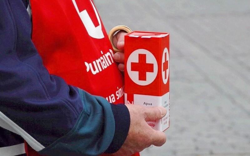 närbild av Röda Korsets insamlingsbössa och en person med röd väst