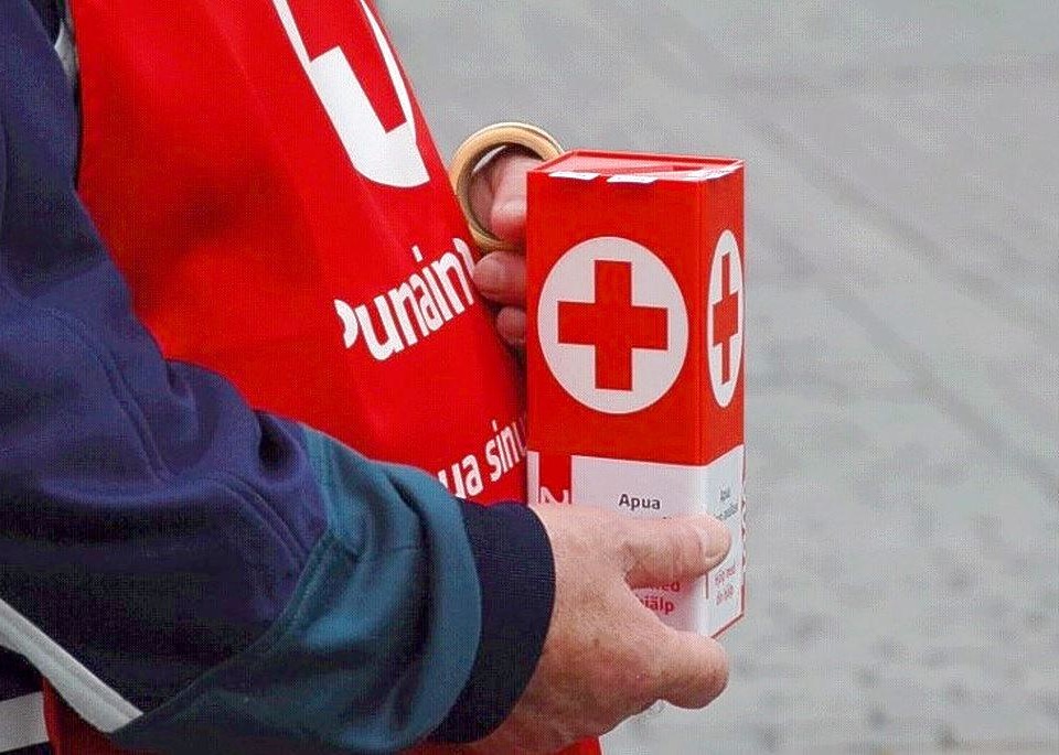 närbild av Röda Korsets insamlingsbössa och en person med röd väst