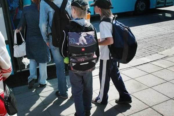 Skolbarn stiger in i en buss, med ryggsäckar på ryggen.