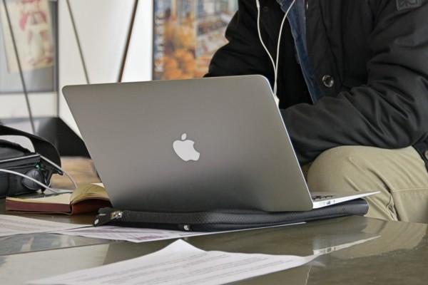 Några papper och en dator på ett bord samt överkroppen av personen som sitter vid datorn.