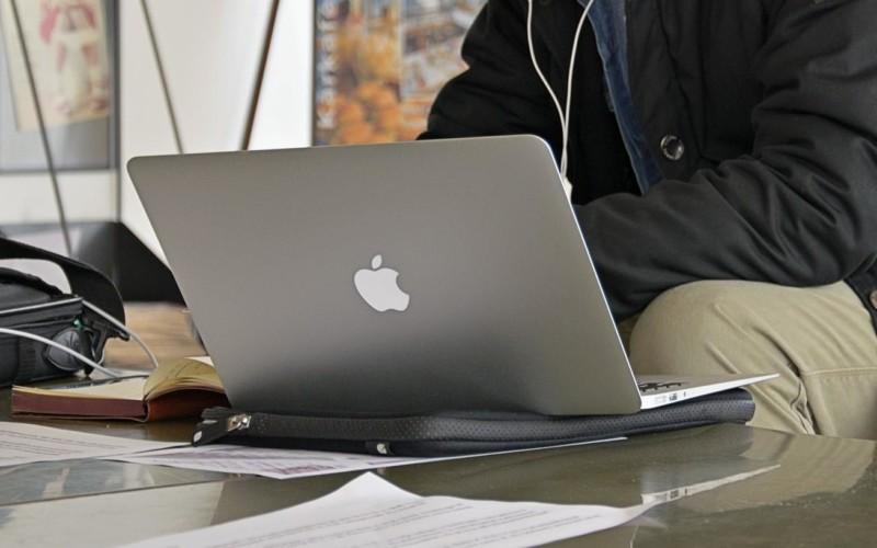 Några papper och en dator på ett bord samt överkroppen av personen som sitter vid datorn.