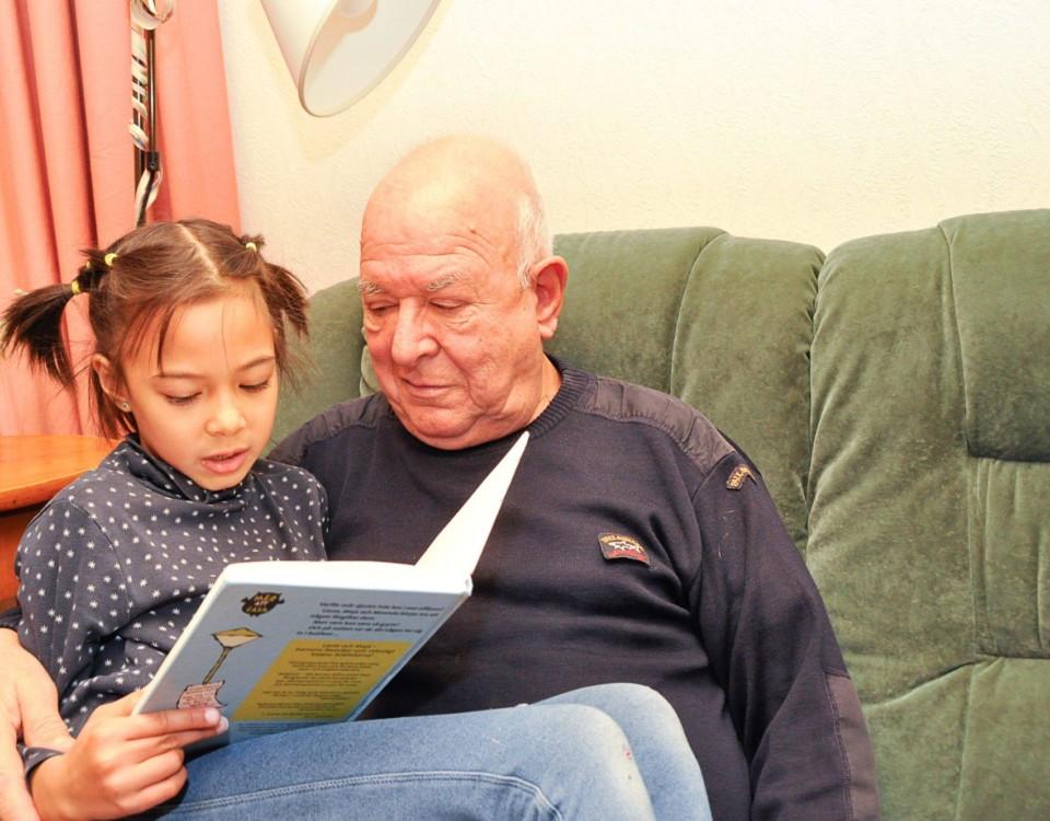 En tjej sitter i sin pappas famn och läser en bok.