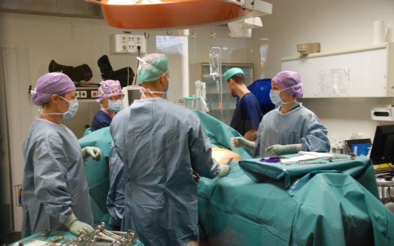 Fem kirurger klädda i skyddskläder står runt ett operationsbord.