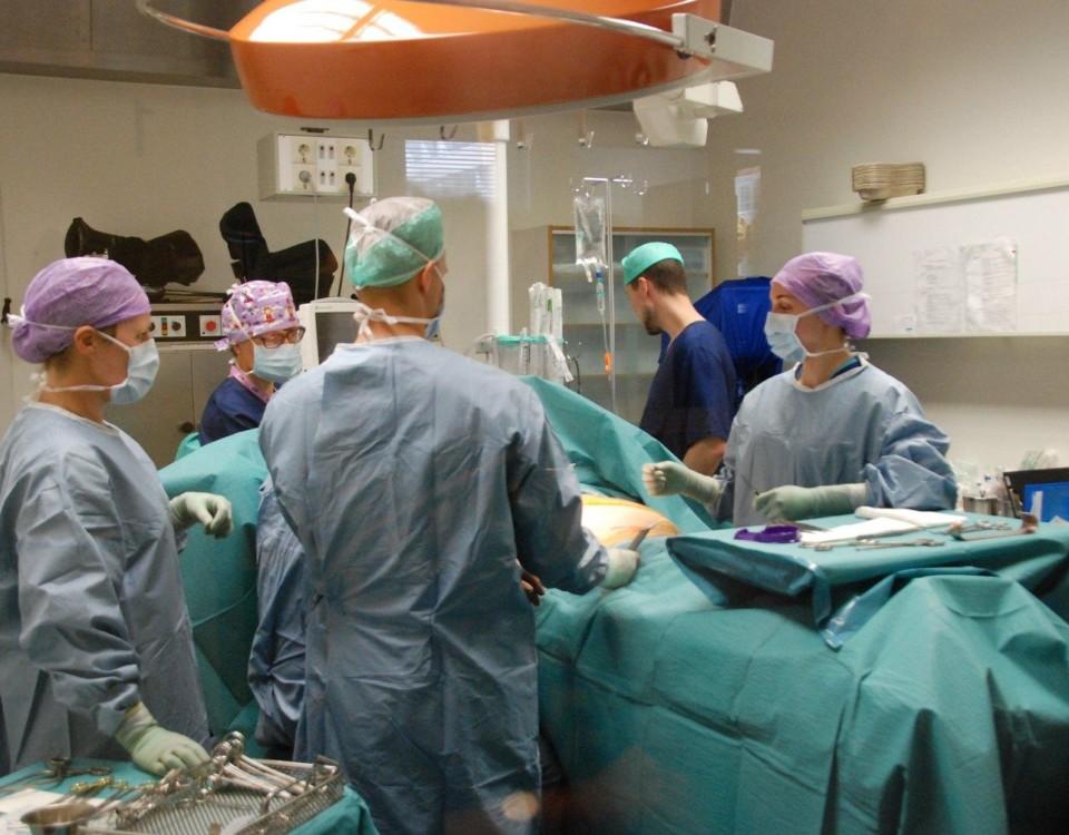 Fem kirurger klädda i skyddskläder står runt ett operationsbord.