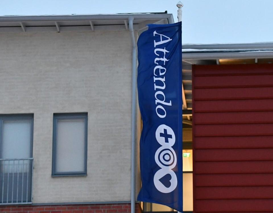 blå lodrätt flagga med texten Attendo på husvägg