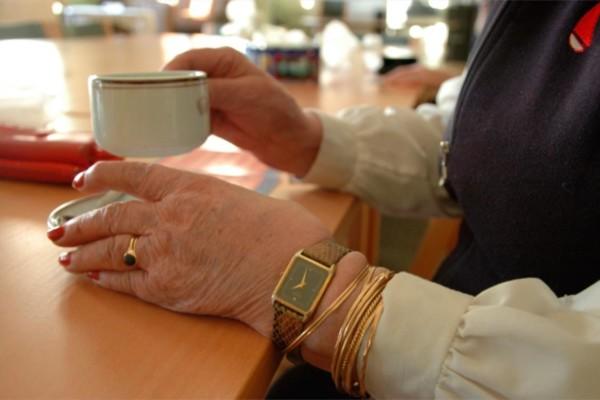 En äldre persons händer som håller i en kaffekopp.