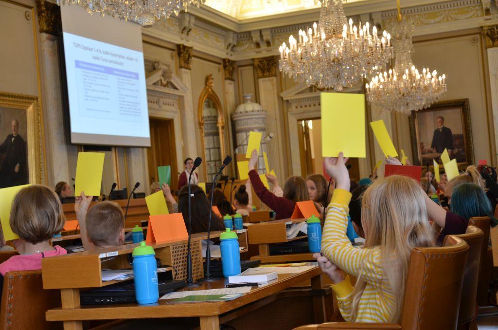 Barn deltar i omröstning genom att räcka upp gula, gröna och röda lappar.