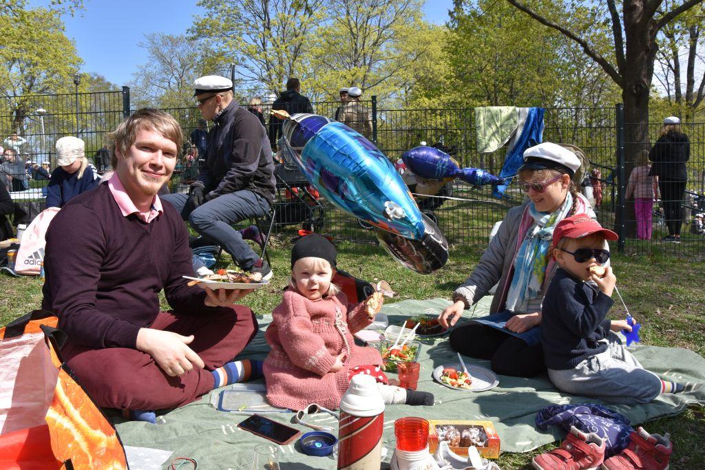 En familj sitter på en picknickfilt i en park.