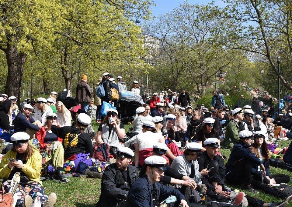 Människor på picknick i en solig och grön park. Många har på sig studentmössor.
