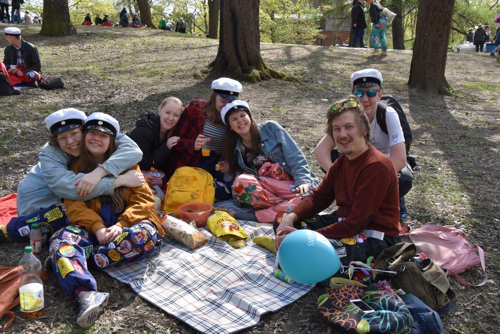 Sju ungdomar sitter på en picknickfilt