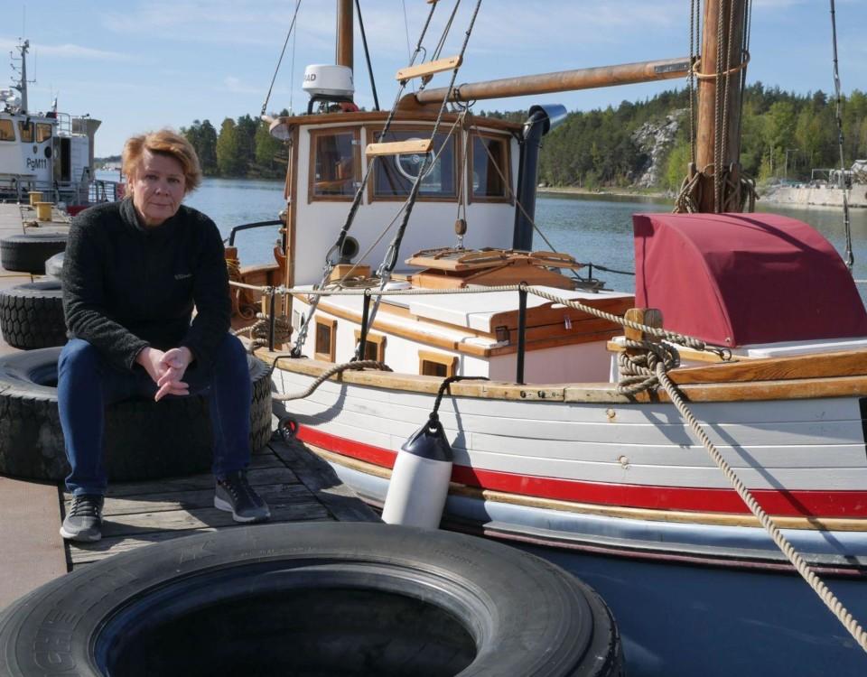 Kvinna sitter på brygga med båtar i bakgrunden