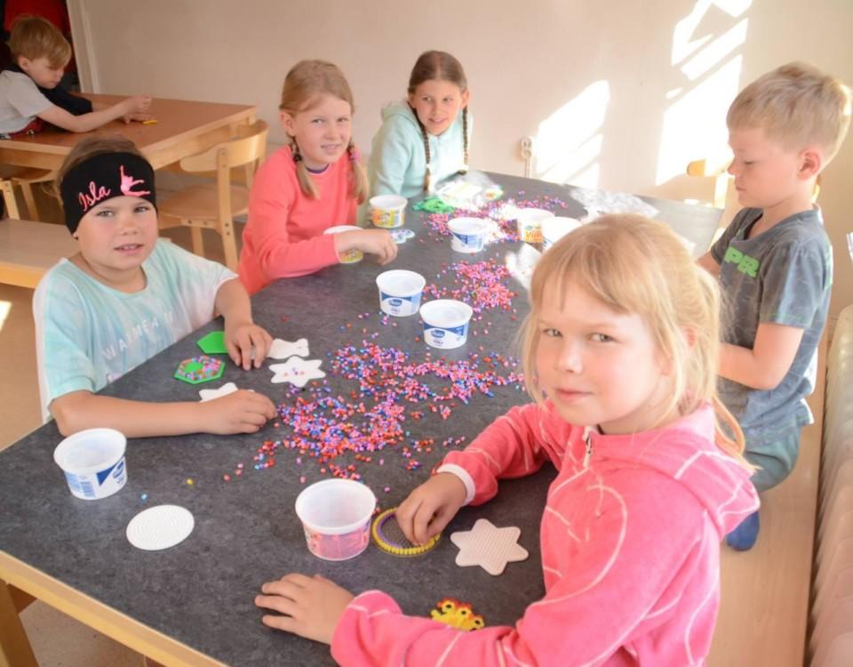 Barn sitter runt ett bord med pärlor.
