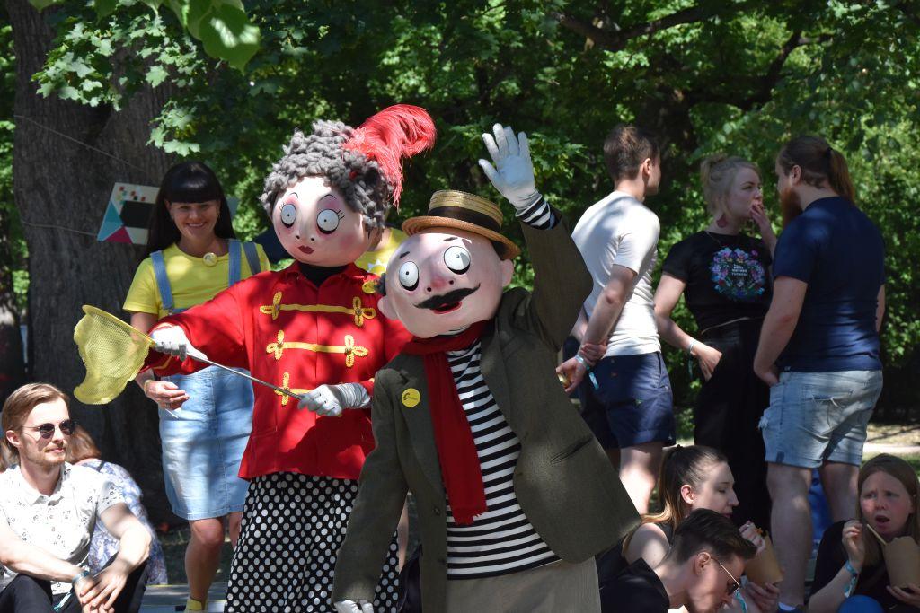 Två personer utklädda till lustiga dockor poserar på ett festivalområde.