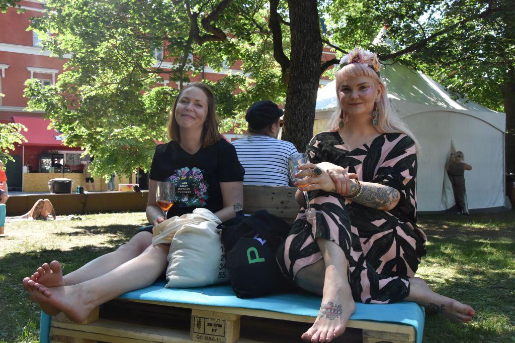 Två kvinnor sitter på lastpallar som gjorts om till soffor med varsitt vinglas i handen