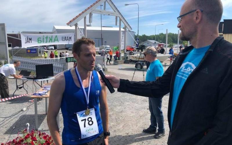 En man i träningskläder, med en medalj om halsen blir intervjuad vid inkörsporten till Kasnäs.