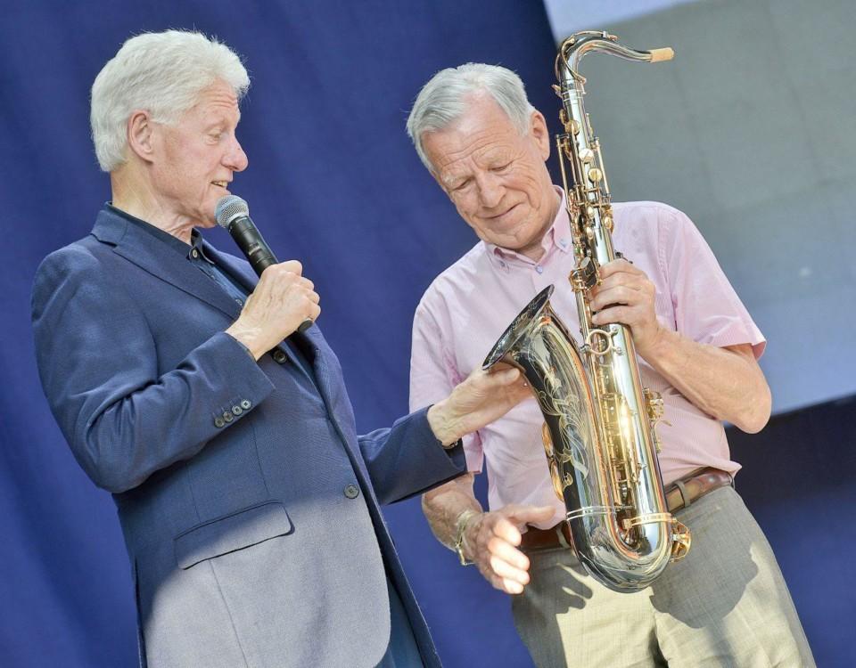 Bill Clinton och Anders Wiklöf står på en scen. Wiklöf överräcker en saxofon till Clinton.