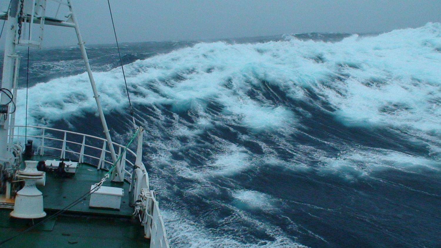 Stora gråa vågor och fören på en båt syns på bilden.