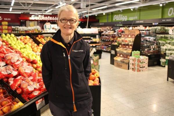 Anne Nyman står vid frukt- och grönskaksavdelningen i K-Supermarket, bredvid äpplena.