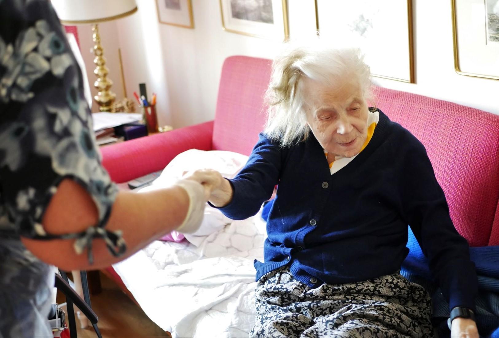 Vårdare håller i äldre persons hand och drar upp henne ur sängen