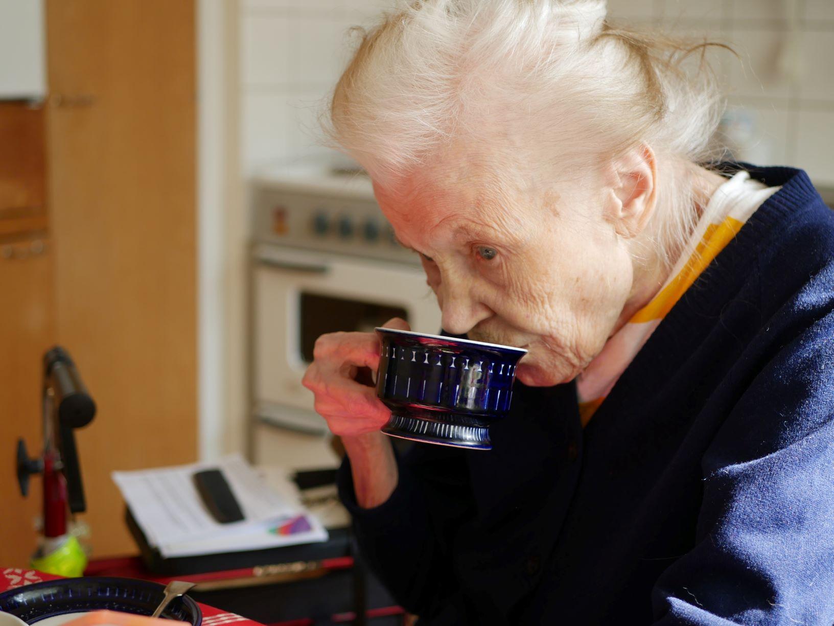 Äldre kvinna dricker kaffe i köket 