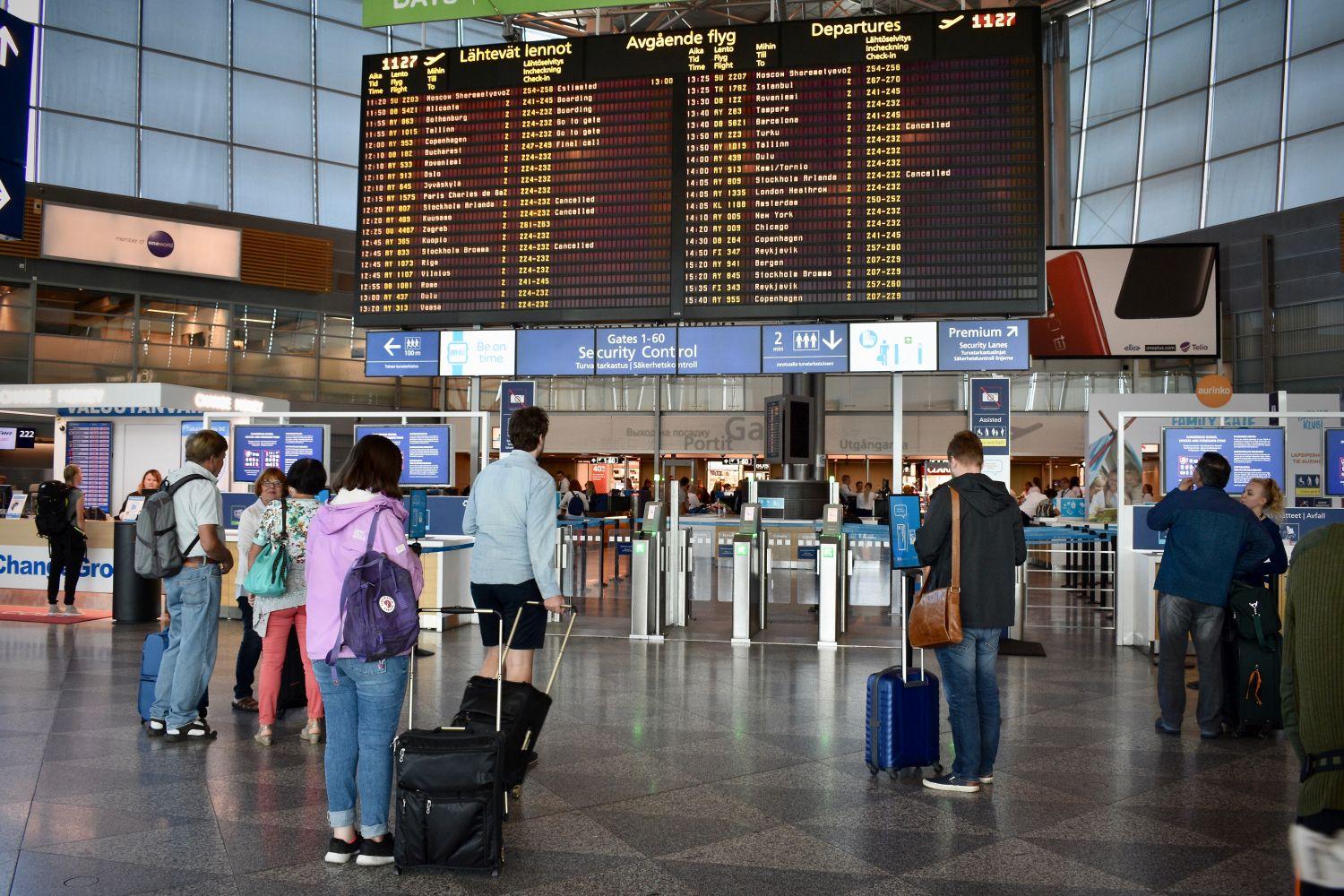 Människor som står framför en skärm med uppgifter om flygtider på en flygplats.