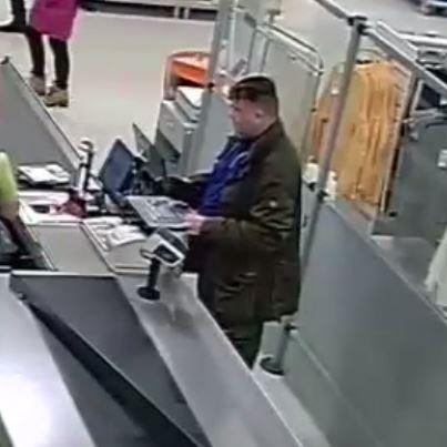 En man står vid en matbutikskassa fotad med övervakningskamera