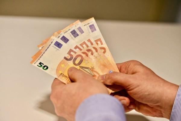 Händer som håller i flera 50 euros sedlar.