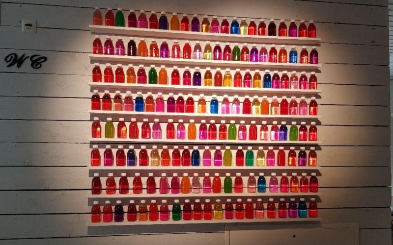 vägg fylld med små glasflaskor på små hyllor fyllda med olika färgers vätskor.