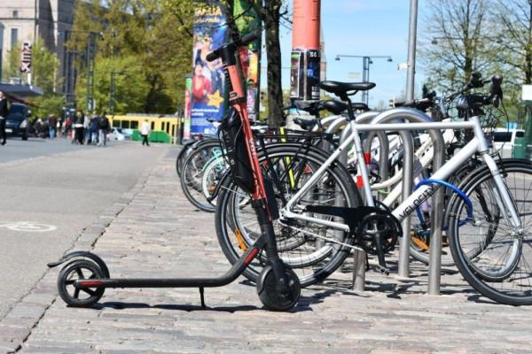 En elsparkcykel står parkerad intill flera cyklar i stadsmiljö.