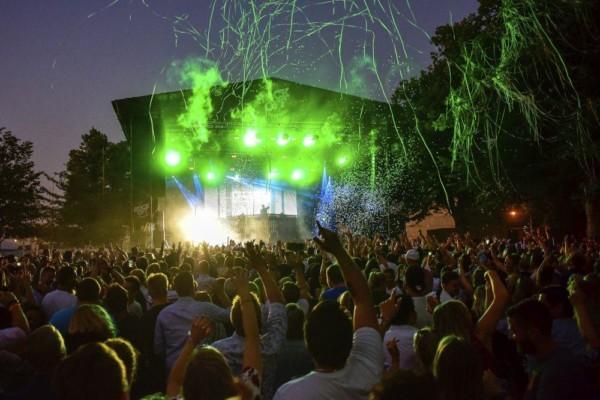 En publik står framför en festivalscen upplyst i grönt med konfetti sprutandes över människomassorna.
