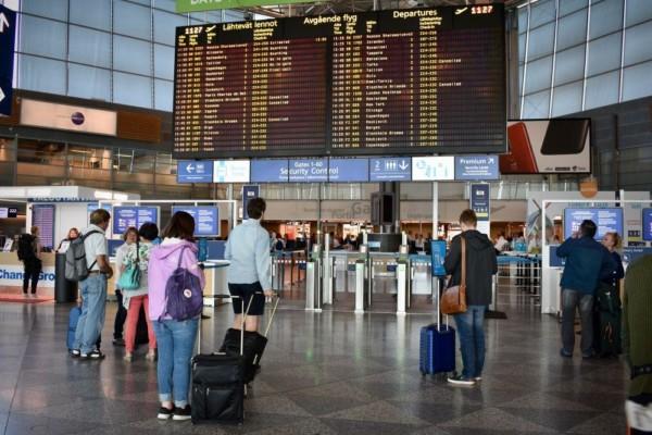 Resenärer står och kollar på skärm med information om avgående flyg på flygfältet.