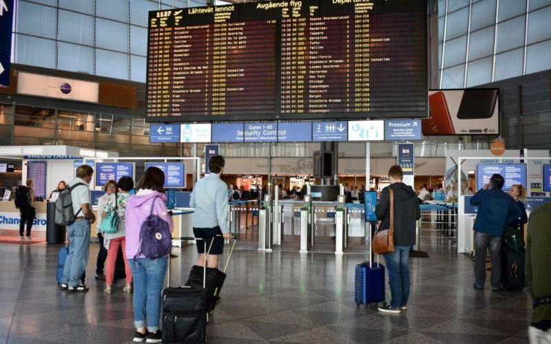 Resenärer står och kollar på skärm med information om avgående flyg på flygfältet.
