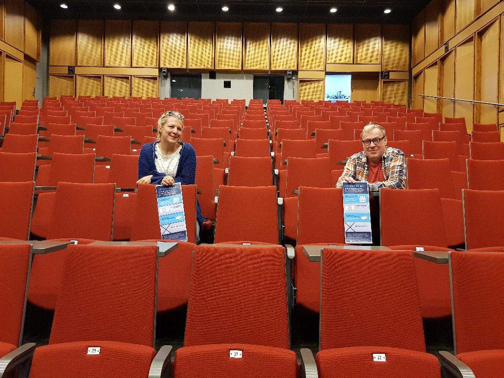 Två personer i ett auditorium med röda stolar