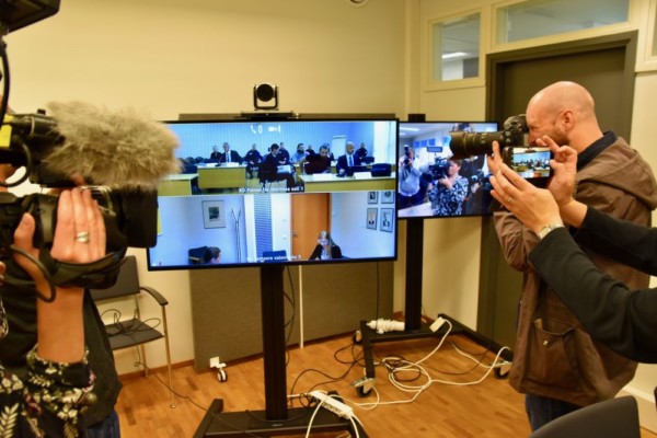 Journalister fotograferar en rättegång via en skärm.