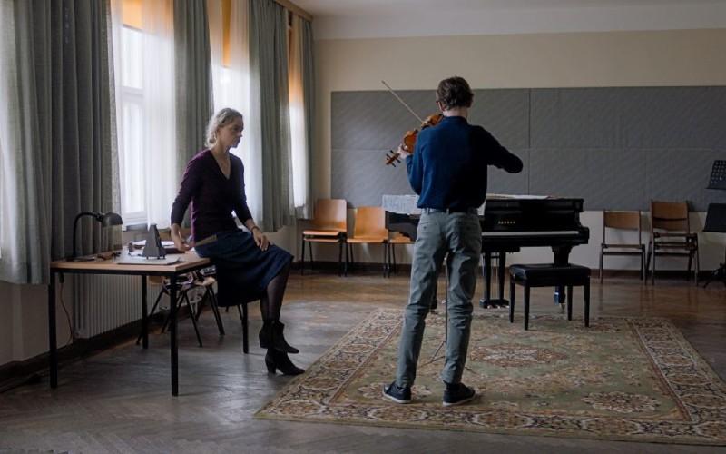 Ur en film. Två personer i ett rum, den ena spelar fiol.