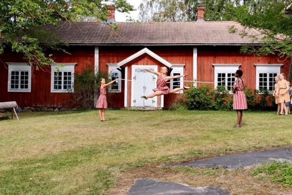Flickor dansar på gräsmattan framför gammalt hus