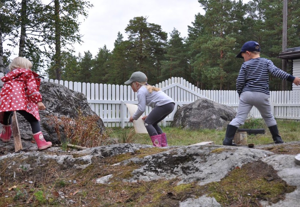 Tre barn leker med träbitar bland stenar på en bakgård, Daghemmet Karusellen i nagu