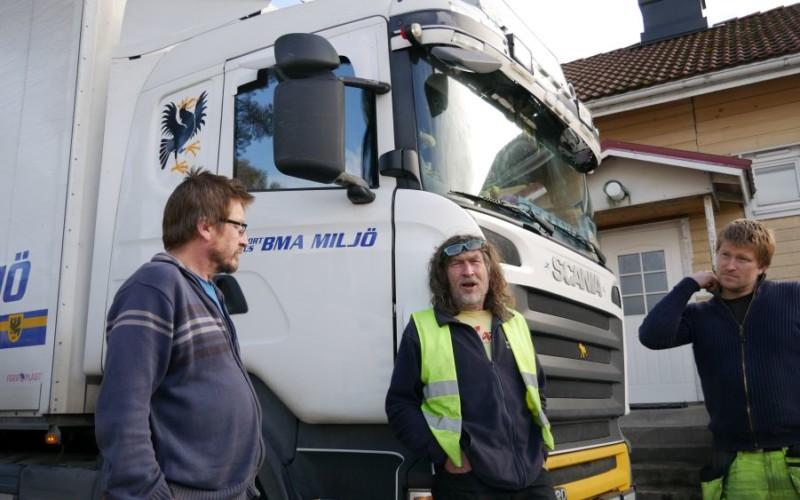 tre män iklädda arbetskläder står framför en lastbil