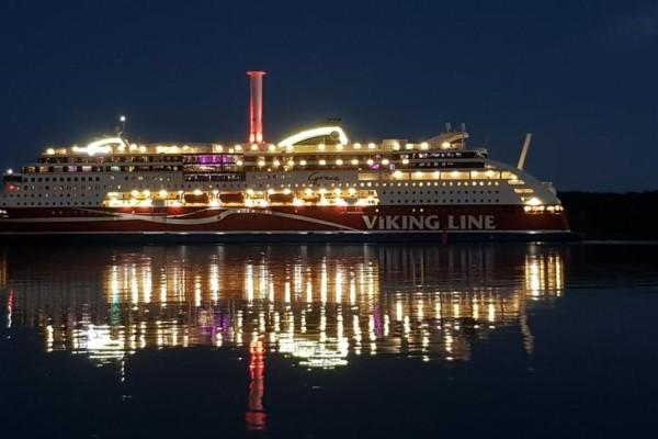 Viking Grace i halvdunkel, med fartygets ljus speglandes i vattenytan.