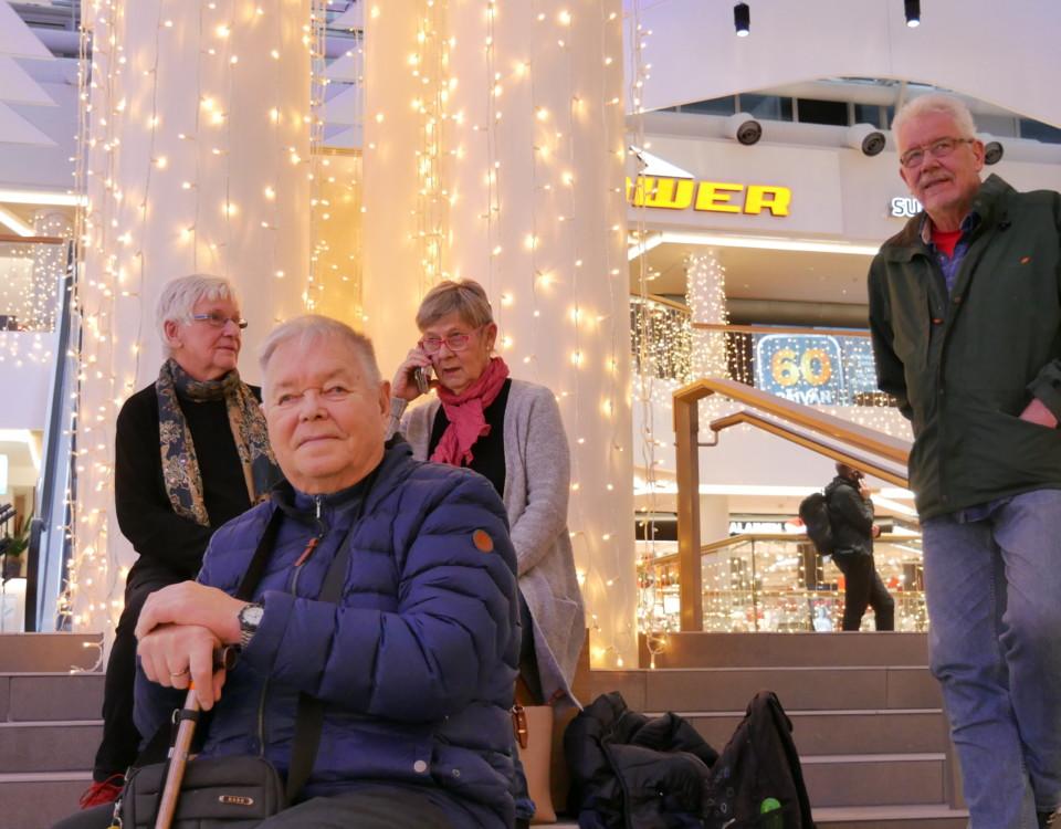 fyra äldre personer sitter tillsammans på en trappa inomhus