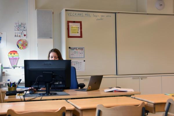 en lärare sitter bakom en datorskärm vid ett skrivbord