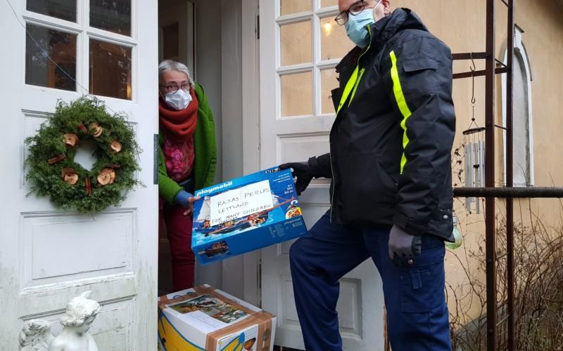 Man och kvinna vid en öppnad dörr till bostadshus. Håller bägge i ett paket. De bär munskydd