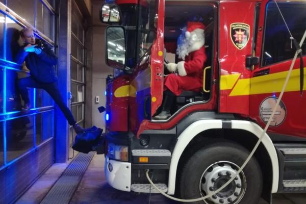 en man står på en brandbils kofångare och filmar julgubben i brandbilen