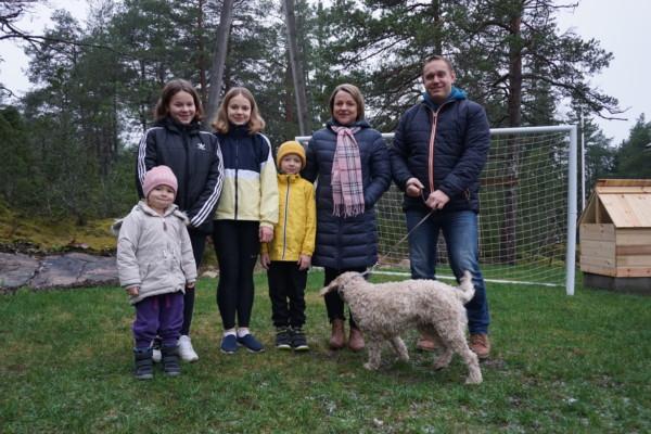 en familj med fyra barn och en hund står på en gräsmatta iklädda vinterkläder