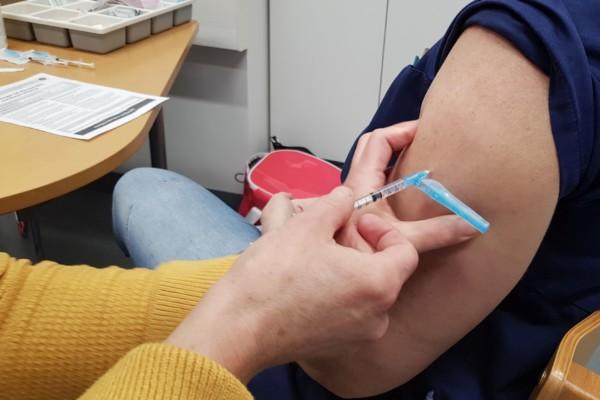 En arm syns, en spruta och händer som sköter vaccineringen