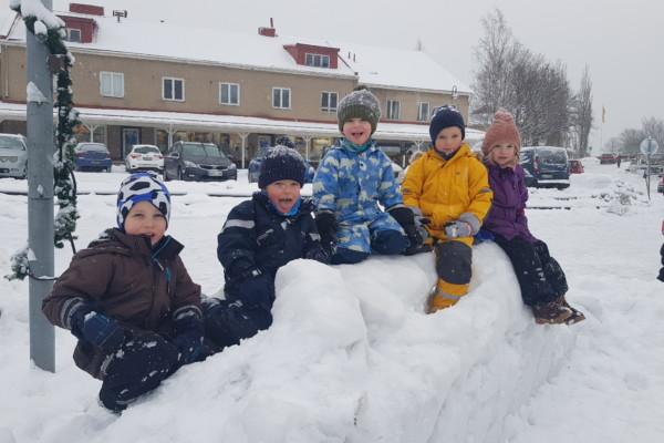 Fem barn i en snöhög på ett torg