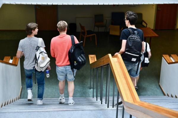 Tre unga killar med ryggsäck på ryggen går nerför en trappa i en skola.