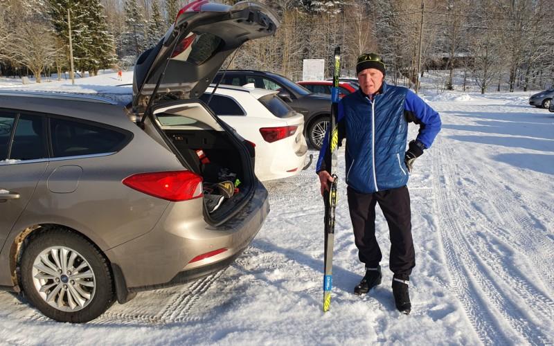 Arto Aunola står vid den öppna bakluckan på sin bil och håller i ett par skidor.
