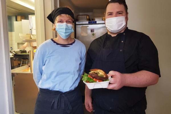 Två personer som jobbar i ett kök poserar med en hamburgare i en liten låda.