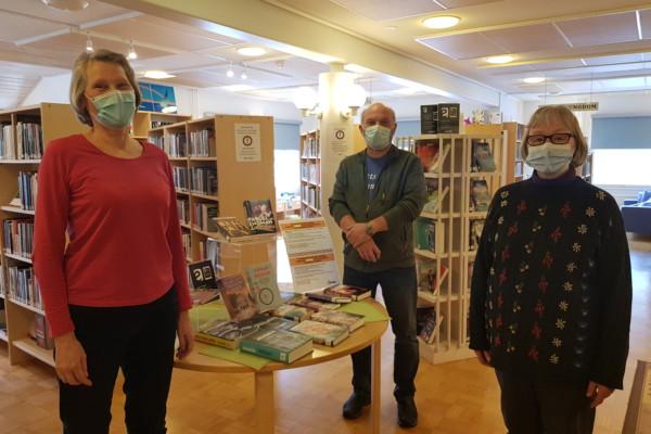 Tre personer med munskydd i ett bibliotek